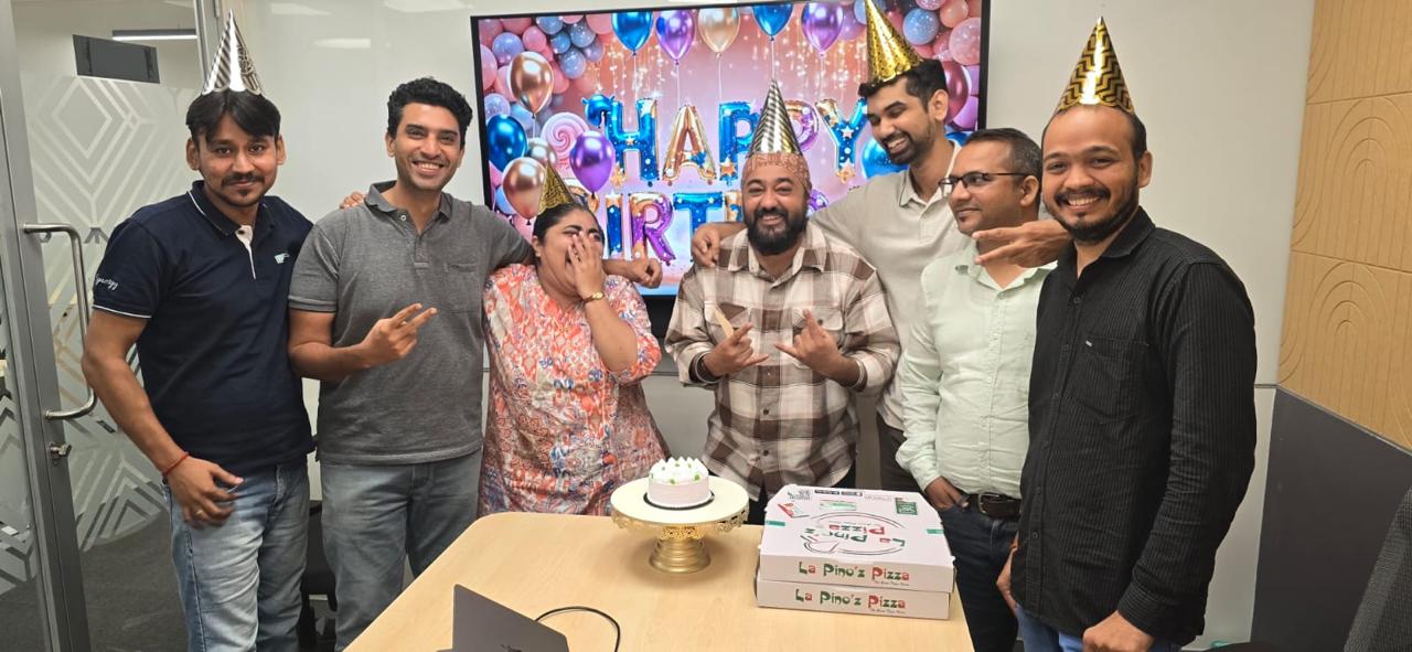 Colleagues in party hats celebrating a birthday with cake and pizza