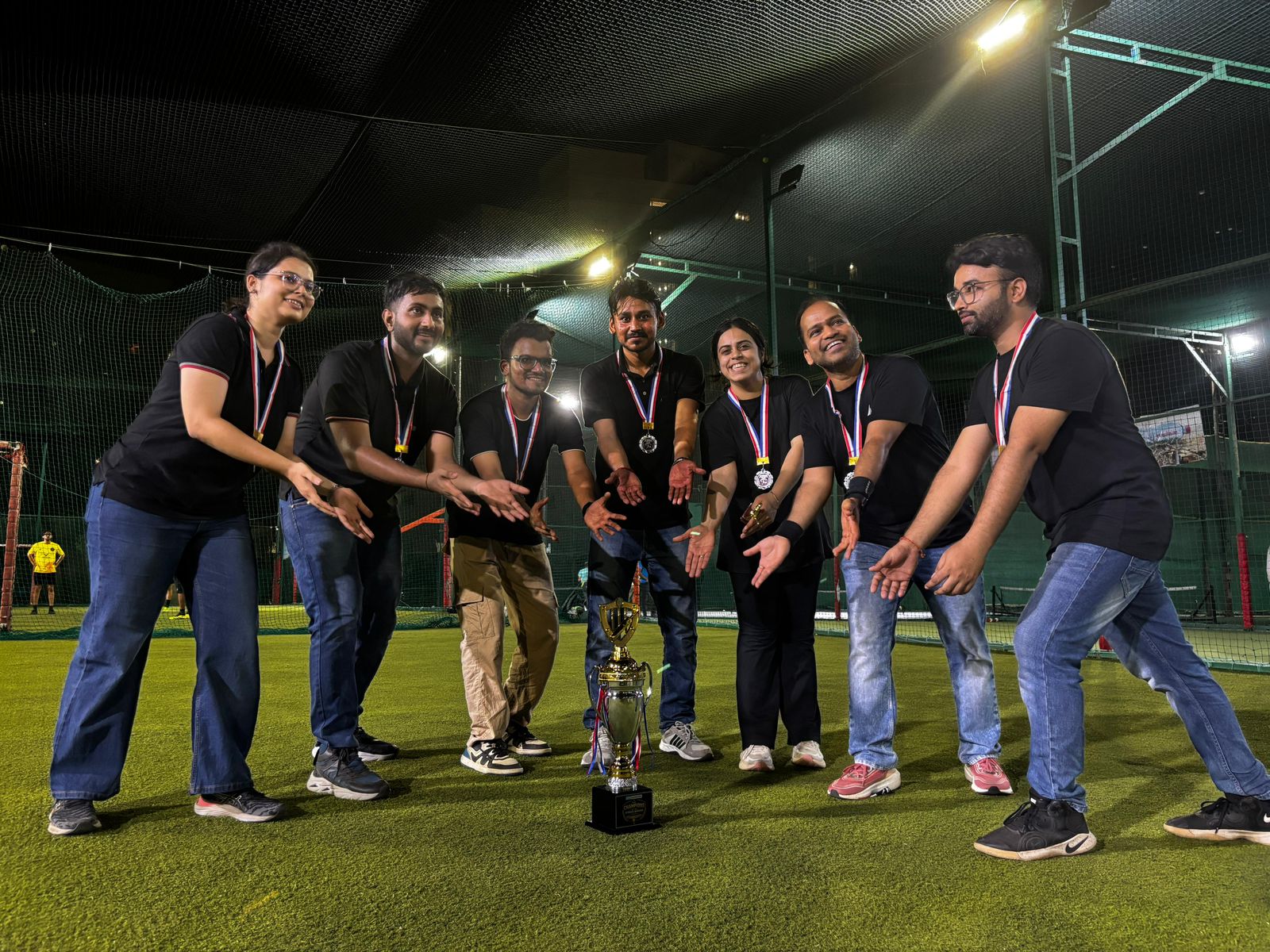 Team in matching black shirts with medals presenting a trophy on turf